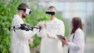 VIDEO Drone filming three laboratory technicians in white coats wearing Virtual Reality headset, working with plants grown with the Hydroponic method in a greenhouse - Starpik