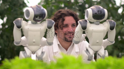 VIDEO Laboratory technician in a white coat interacting with two humanoid robots near different types of lettuce in a greenhouse farm - Starpik