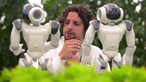 VIDEO Laboratory technician in a white coat interacting with two humanoid robots near different types of lettuce in a greenhouse farm - Starpik