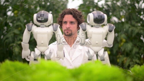 VIDEO Laboratory technician in a white coat interacting with two humanoid robots near different types of lettuce in a greenhouse farm - Starpik