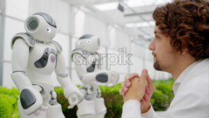 VIDEO Laboratory technician in a white coat interacting with two humanoid robots near different types of lettuce in a greenhouse farm - Starpik