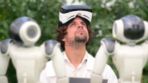 VIDEO Laboratory technician in a white coat with virtual reality headset looking around near humanoid robot in a greenhouse farm - Starpik