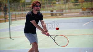 VIDEO Man in black shirt playing tennis on a blue and green court on a sunny day - Starpik