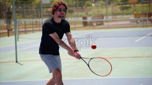 VIDEO Man in black shirt playing tennis on a blue and green court on a sunny day - Starpik