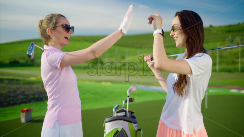 VIDEO Two woman holding golf clubs on their shoulders and high fiving each other on a sunny day - Starpik