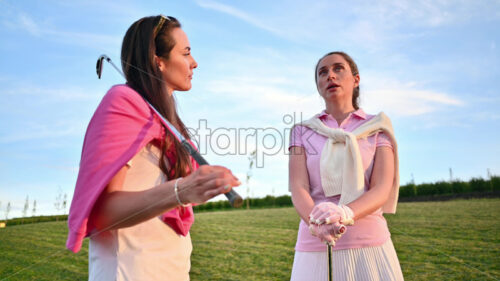 VIDEO Two women dressed in white and pink clothes, holding golf clubs and talking on the course - Starpik