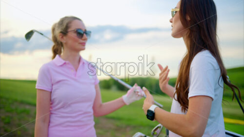 VIDEO Two women dressed in white and pink clothes, holding golf clubs and talking on the course - Starpik