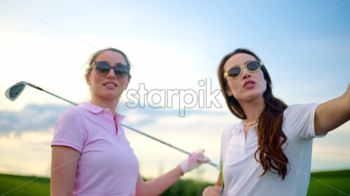 VIDEO Two women dressed in white and pink clothes, holding golf clubs and talking on the course - Starpik