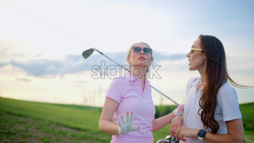 VIDEO Two women dressed in white and pink clothes, holding golf clubs and talking on the course - Starpik