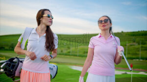 VIDEO Two women dressed in white and pink clothes, holding golf clubs, walking and talking on the golf course - Starpik