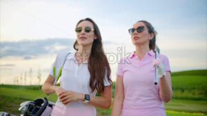 VIDEO Two women dressed in white and pink clothes, holding golf clubs, walking and talking on the golf course - Starpik