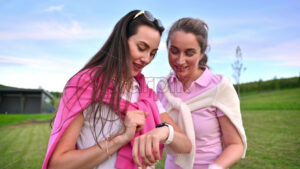 VIDEO Two women dressed in white and pink clothes touching a smart watch and talking on the golf course - Starpik