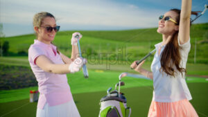 VIDEO Two women dressed in white and pink clothes, with golf clubs on their shoulders, laughing on the golf course - Starpik