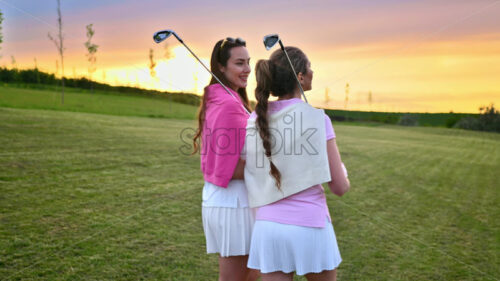 VIDEO Two women dressed in white and pink clothes, with golf clubs on their shoulders, walking and talking on the golf course - Starpik