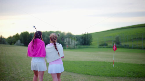 VIDEO Two women dressed in white and pink clothes, with golf clubs on their shoulders, walking and talking on the golf course - Starpik