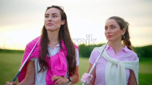 VIDEO Two women dressed in white and pink clothes, with golf clubs on their shoulders, walking and talking on the golf course - Starpik