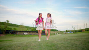 VIDEO Two women dressed in white and pink clothes, with golf clubs on their shoulders, walking and talking on the golf course - Starpik