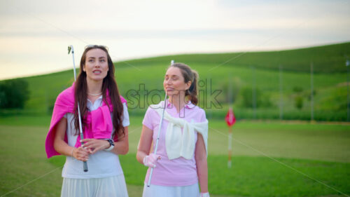 VIDEO Two women dressed in white and pink clothes, with golf clubs on their shoulders, walking and talking on the golf course - Starpik