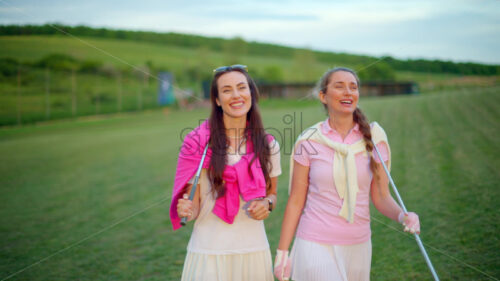 VIDEO Two women dressed in white and pink clothes, with golf clubs on their shoulders, walking and talking on the golf course - Starpik