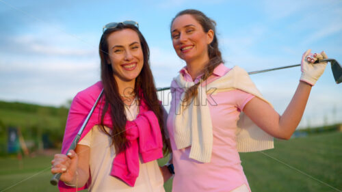 VIDEO Two women in white and pink clothes, posing with golf clubs in their hands, on a grass field - Starpik