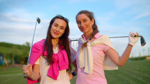 VIDEO Two women in white and pink clothes, posing with golf clubs in their hands, on a grass field - Starpik