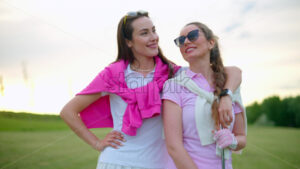 VIDEO Two women in white and pink clothes, standing and holding golf clubs, on a grass field - Starpik