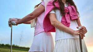 VIDEO Two women in white and pink clothes, standing back to back with golf clubs in their hands, on a grass field - Starpik