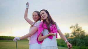 VIDEO Two women in white and pink clothes, standing back to back with golf clubs in their hands, on a grass field - Starpik