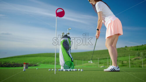 VIDEO Woman dressed in white and pink playing golf near a cart bag on the course - Starpik