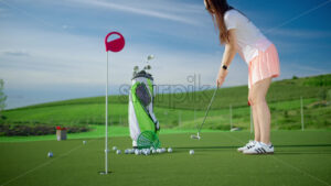 VIDEO Woman dressed in white and pink playing golf near a cart bag on the course - Starpik