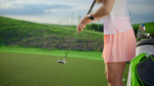 VIDEO Woman dressed in white and pink practicing golf near a cart bag on the course - Starpik