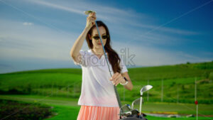 VIDEO Woman dressed in white and pink putting a golf club in a cart bag on the course - Starpik