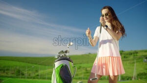 VIDEO Woman dressed in white and pink taking out a golf club from a cart bag on the course - Starpik