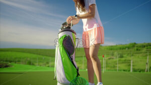 VIDEO Woman dressed in white and pink taking out a golf club from a cart bag on the course - Starpik