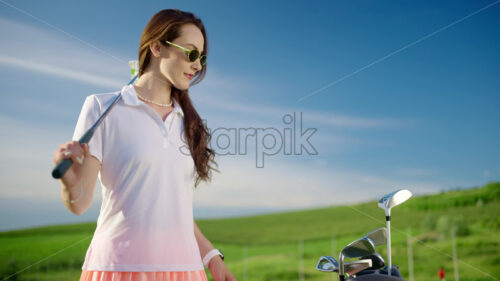 VIDEO Woman dressed in white and pink taking out a golf club from a cart bag on the course - Starpik