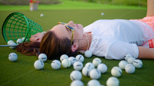 VIDEO Woman lying on the golf course near a bucket with spilled balls - Starpik