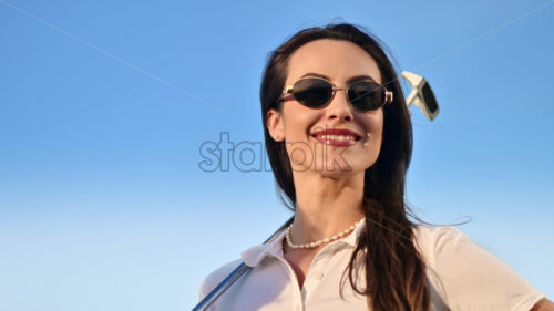 VIDEO Woman wearing sunglasses, holding a golf club on her shoulder with the blue sky on the background - Starpik