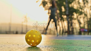 VIDEO Yellow ball on a blue and green court with a woman playing pickleball at sunrise, after rain on the background - Starpik