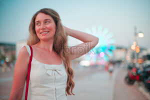 Happy woman in white summer dress posing in front of Cannes rotating wheel, France - Starpik