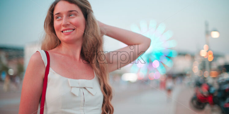 Happy woman in white summer dress posing in front of Cannes rotating wheel, France - Starpik