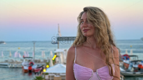 Royalty free stock video Woman in pink dress posing with the beach on the background in the evening in Cannes, France - Starpik