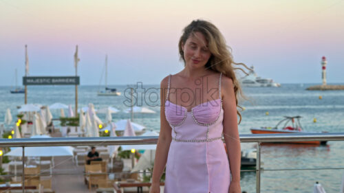 Royalty free stock video Woman in pink dress posing with the beach on the background in the evening in Cannes, France - Starpik