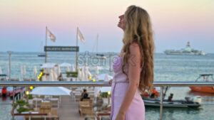 Royalty free stock video Woman in pink dress posing with the beach on the background in the evening in Cannes, France - Starpik