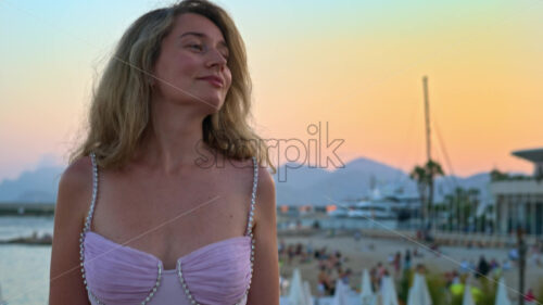 Royalty free stock video Woman in pink dress posing with the beach on the background in the evening in Cannes, France - Starpik