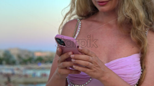 Royalty free stock video Woman in pink dress scrolling on her phone at the beach in the evening in Cannes, France - Starpik