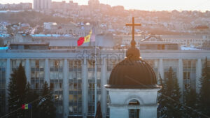 Aerial drone view of Moldova national flag and the Government House at sunset. Golden crosses on top of the Bell tower and the Metropolitan Cathedral of Christ’s Nativity in foreground. Snowy Chisinau - Starpik