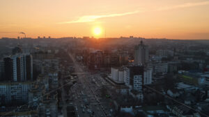 Aerial drone view of city at sunset. Multiple residential and commercial buildings, roads with multiple cars, walking people. Bare trees, winter - Starpik