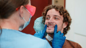 Video Dentist wearing a protective mask, goggles, and gloves checking the teeth of a patient in a dental cabinet - Starpik