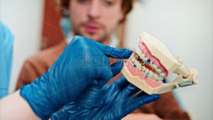 Video Dentist wearing a protective mask, goggles, and gloves showing a teeth mock up to a patient in a dental cabinet - Starpik