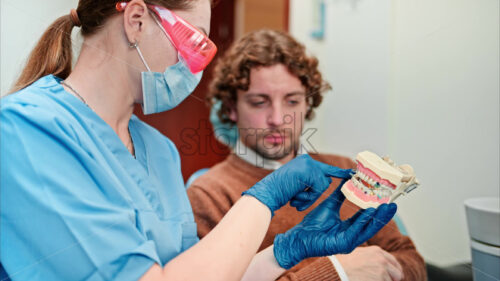 Video Dentist wearing a protective mask, goggles, and gloves showing a teeth mock up to a patient in a dental cabinet - Starpik